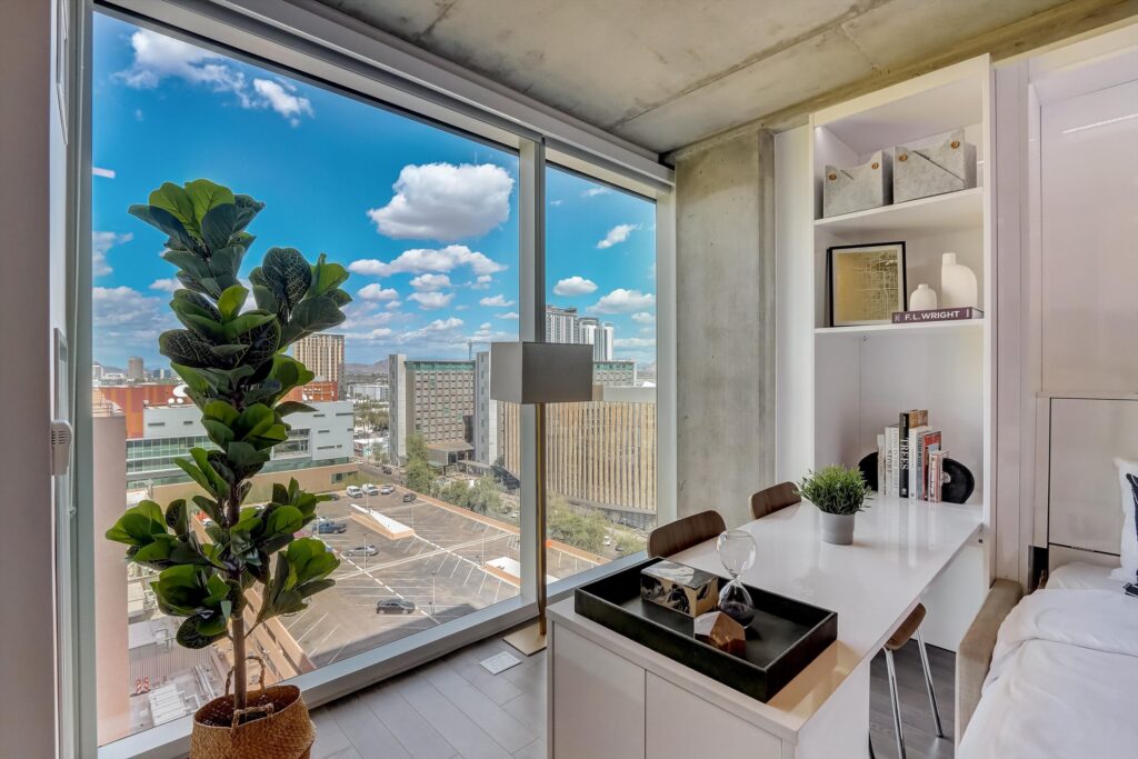 A modern Kenect Phoenix apartment with floor-to-ceiling windows offering a stunning view of downtown Phoenix, including nearby buildings and a clear blue sky.