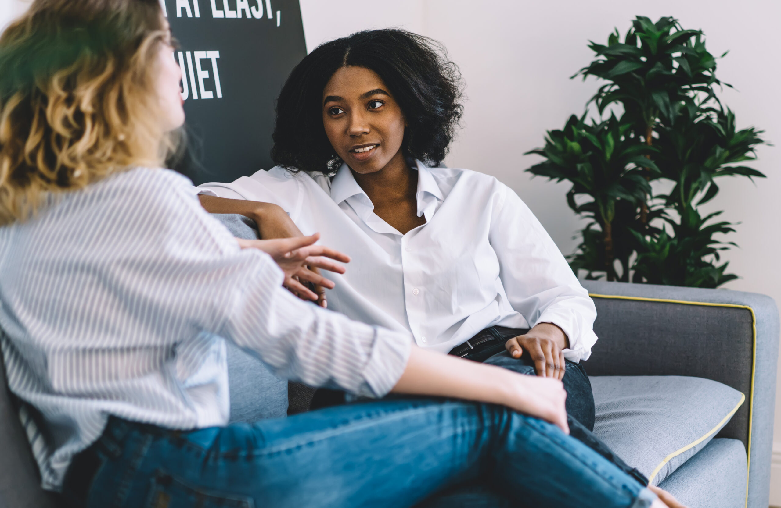 Two female roommates discuss their preferences while sitting on a couch in their shared living space.