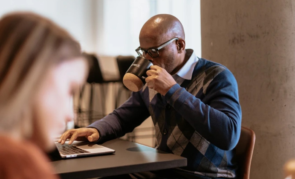 A man drinking coffee while looking at his laptop